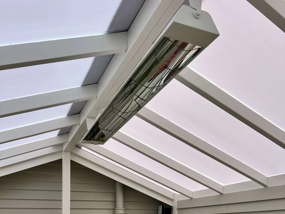 Stainless infrared heater mounted under the rafters of a clear-roofed pergola