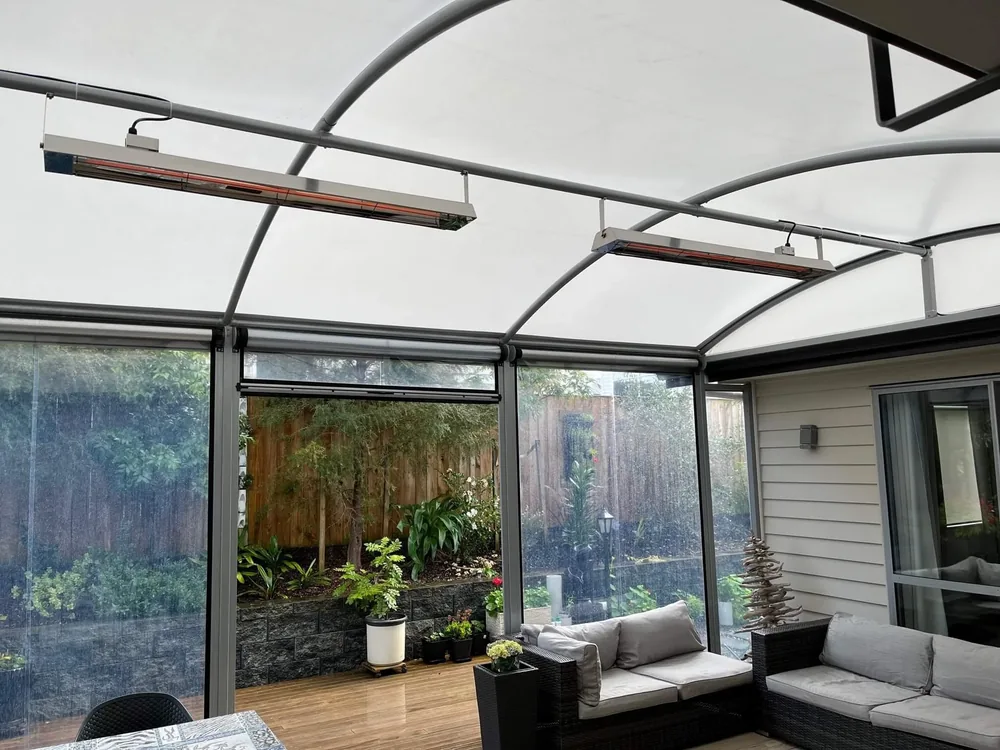 Two heaters hung from a curved roof over an enclosed outdoor lounge