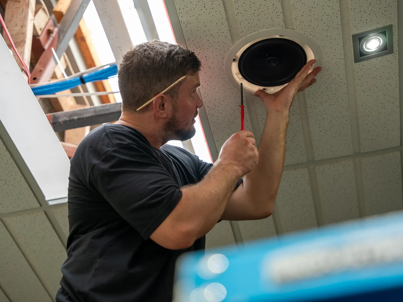 Electrician fitting a round in-ceiling speaker into a suspended office ceiling