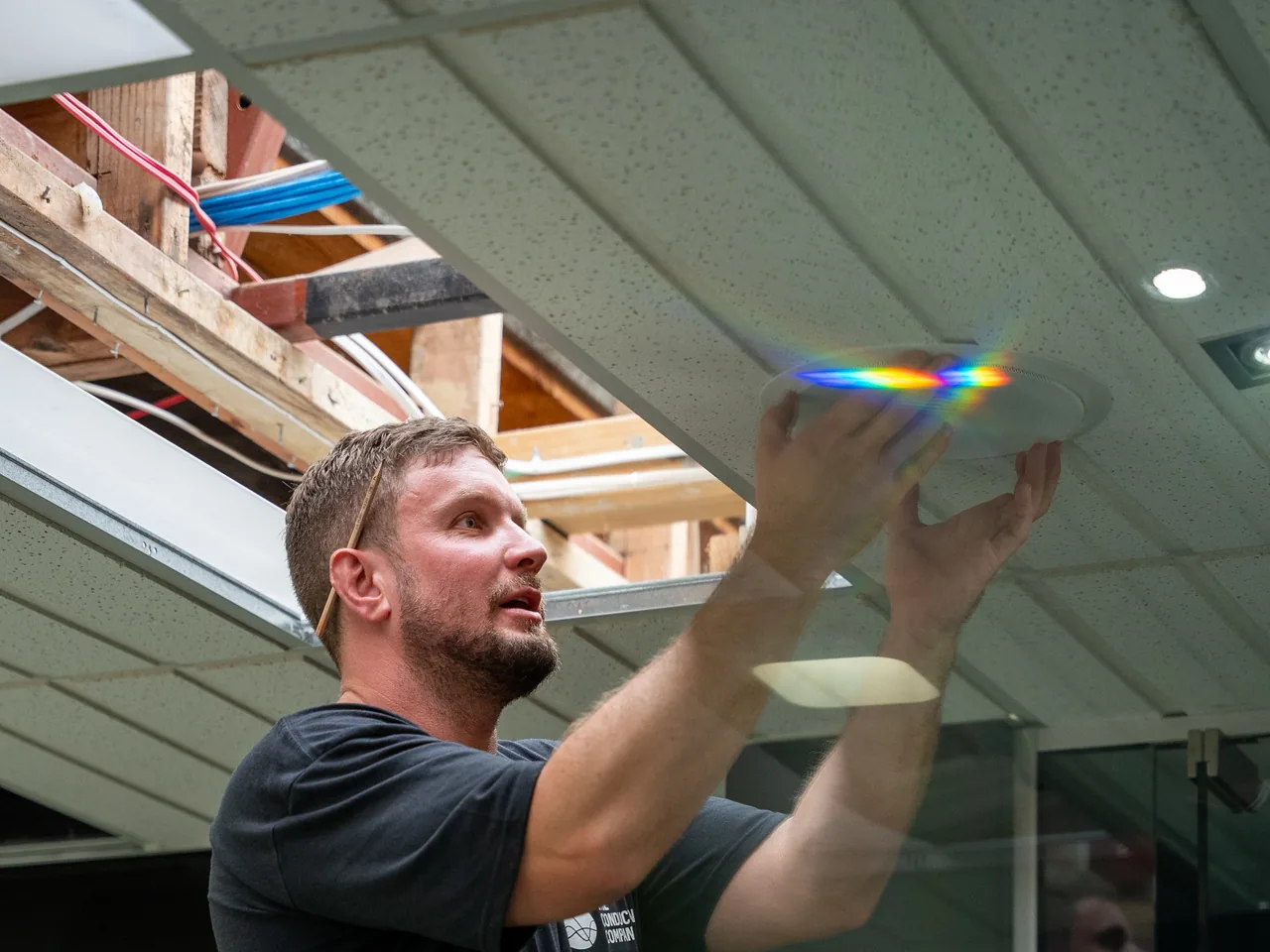 Electrician lifting a round in-ceiling speaker into a suspended office ceiling