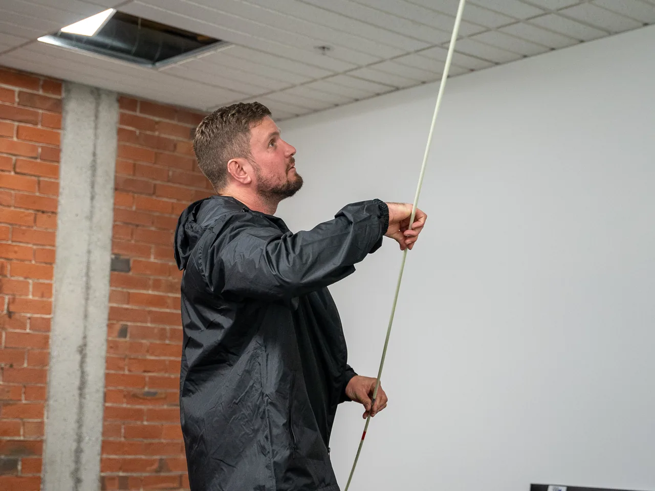 Electrician pushing a cable rod up through an open ceiling tile in an office