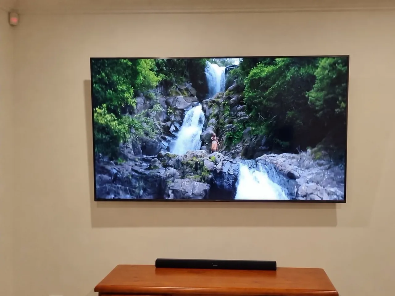 Television mounted on a wall above a timber cabinet with a soundbar on top