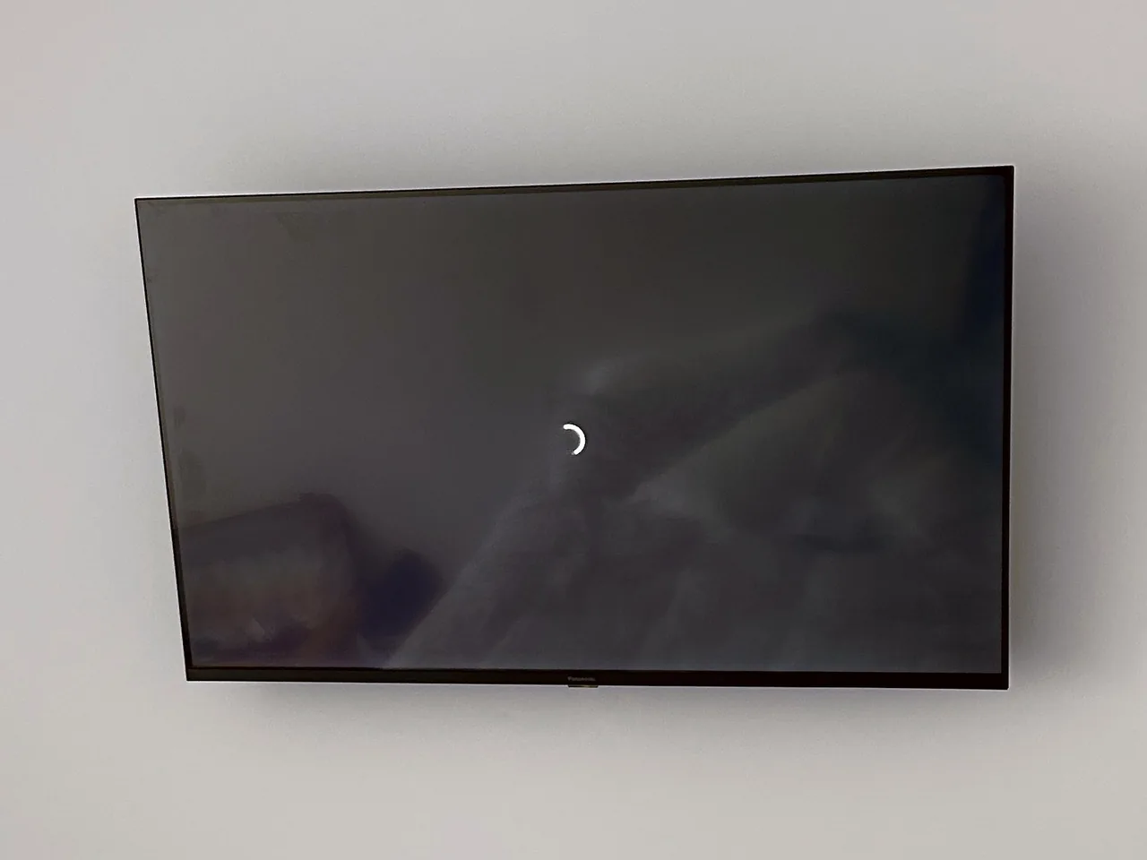 Television mounted high on a plain bedroom wall, screen off, no cables visible