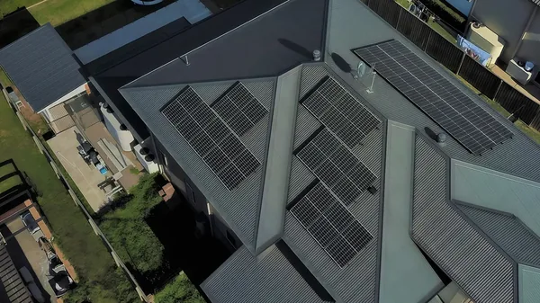 An aerial view of rows of solar panels mounted across a grey metal roof.