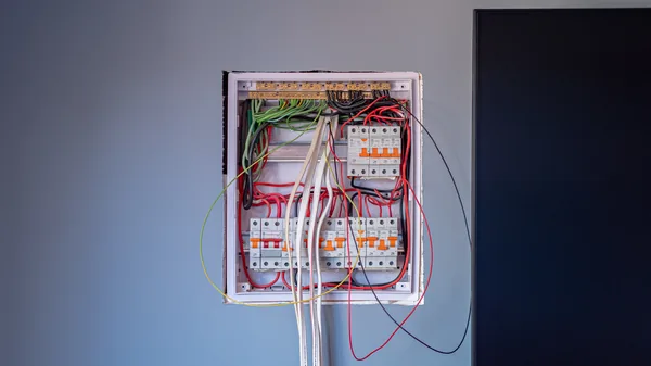 A recessed switchboard set into a cut wall opening mid-installation, with breakers fitted and cables still hanging loose