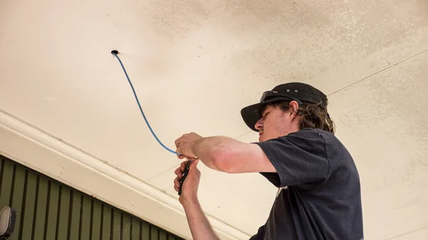 An electrician stripping the end of a blue camera cable where it comes out of a soffit.