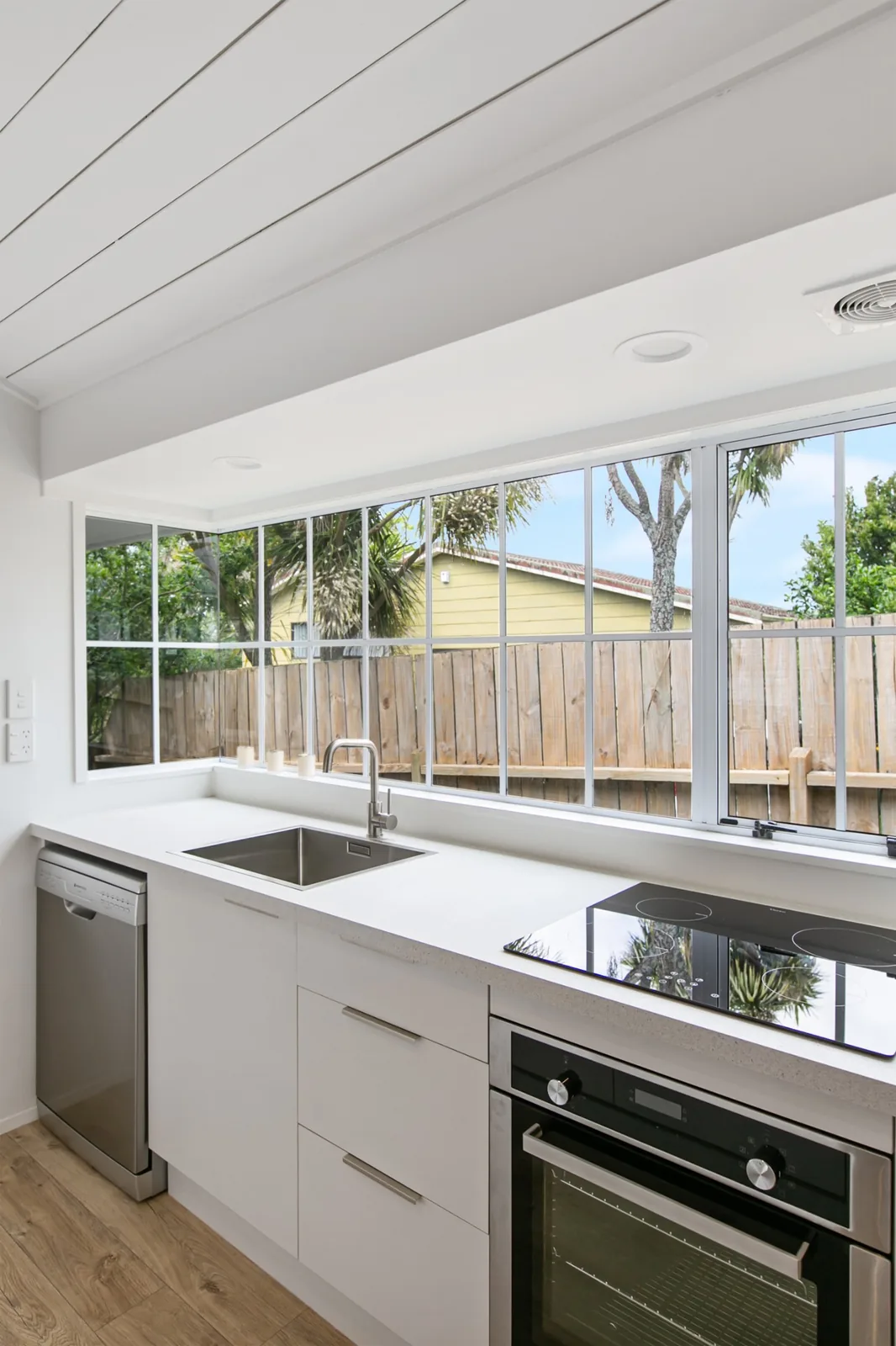 Induction hob, wall oven, and dishwasher under a window, with downlights and an extractor grille in the bulkhead