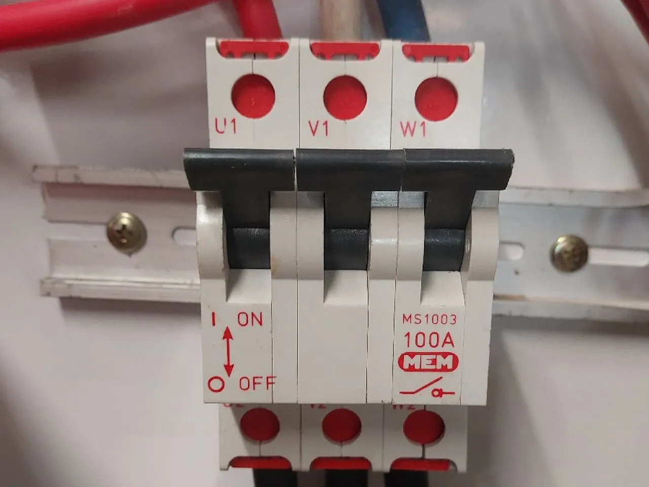 Three-pole 100 amp main switch with its poles marked U1, V1 and W1, thick cables entering above and leaving below