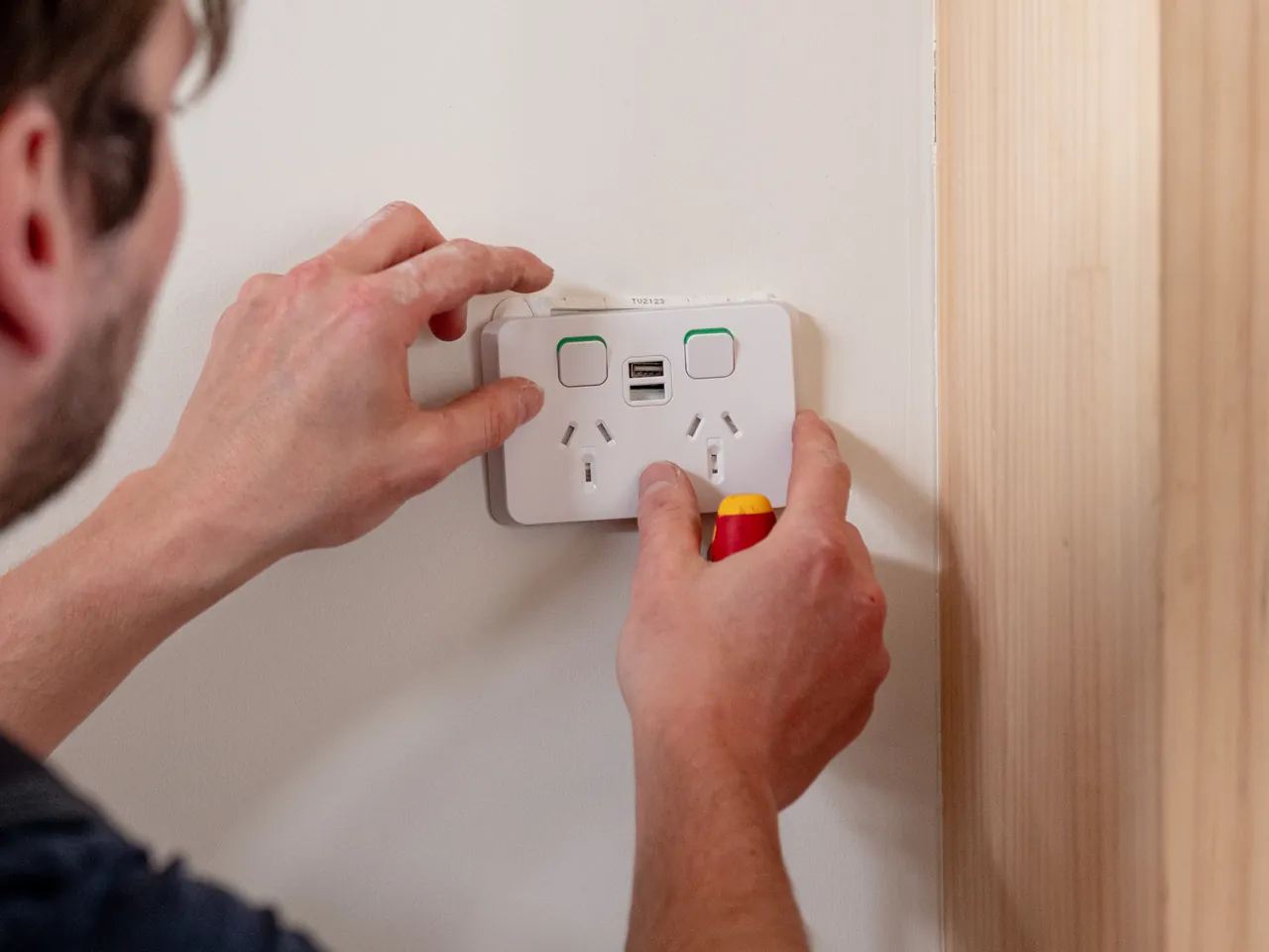Electrician screwing a double power point with USB sockets onto a finished wall
