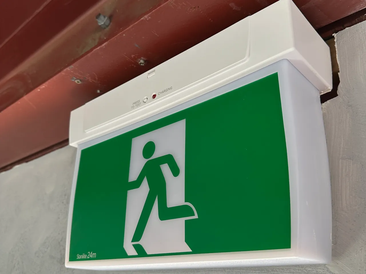 Green running man exit sign fixed under a red steel beam