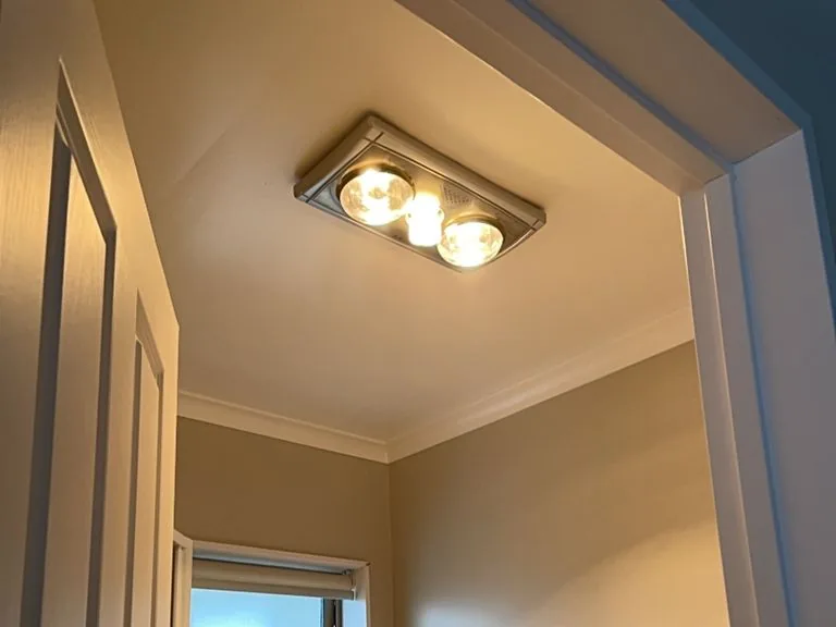 A ceiling unit with two glowing heat lamps and a centre light in a small bathroom
