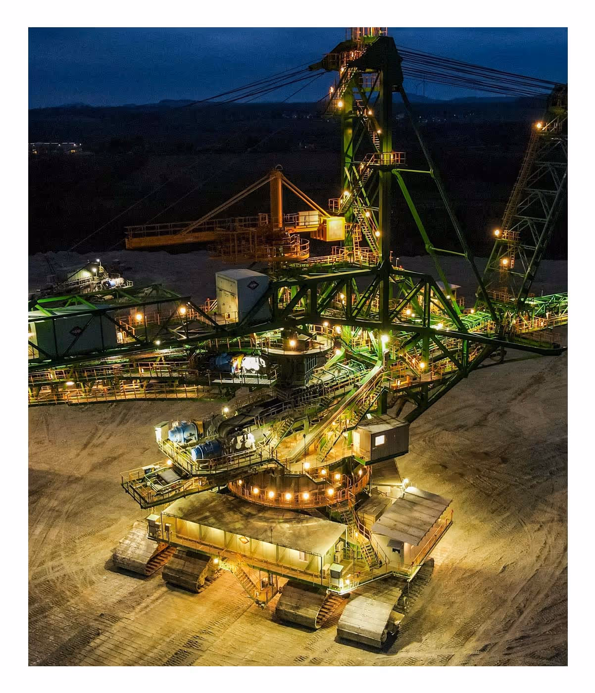 Large green mining excavator with lights operating at night on a sandy mining site.