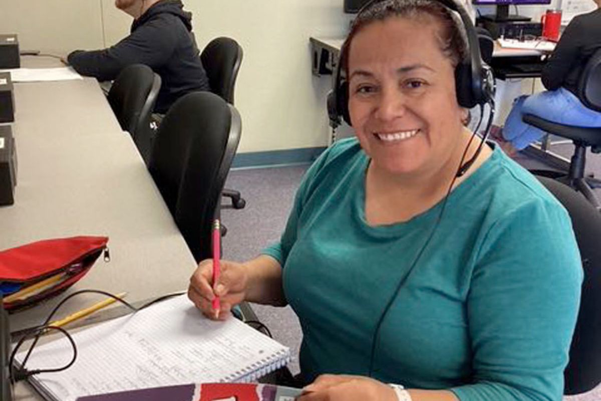 Smiling woman wearing headset writing in notebook at office workspace