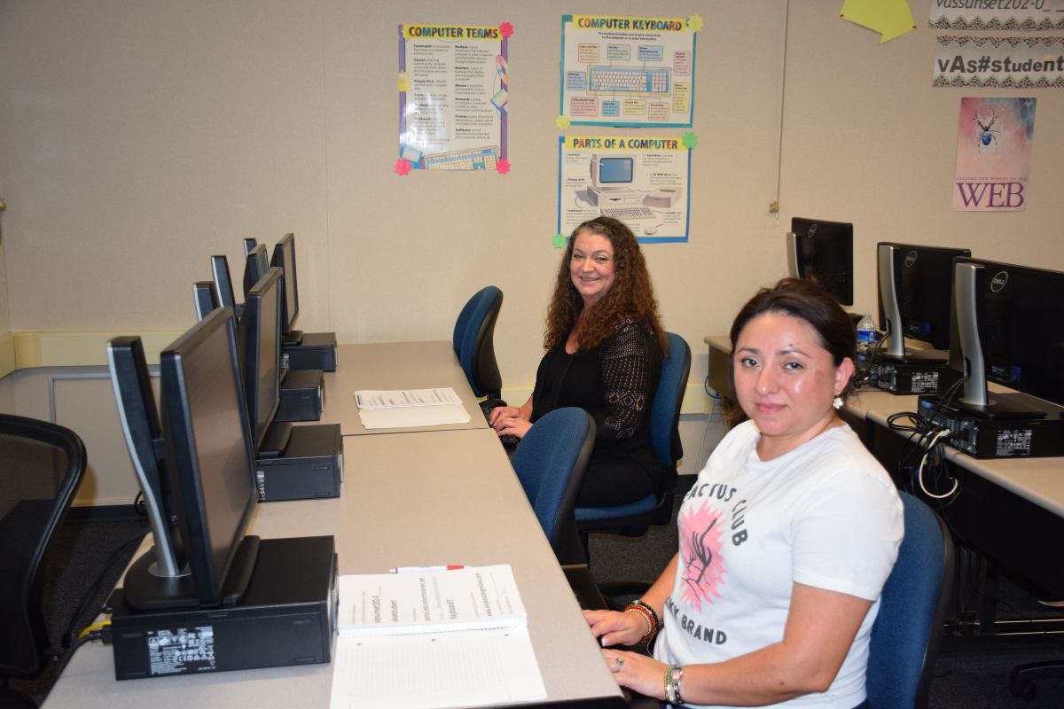 Two women working in computer lab with educational posters on wall