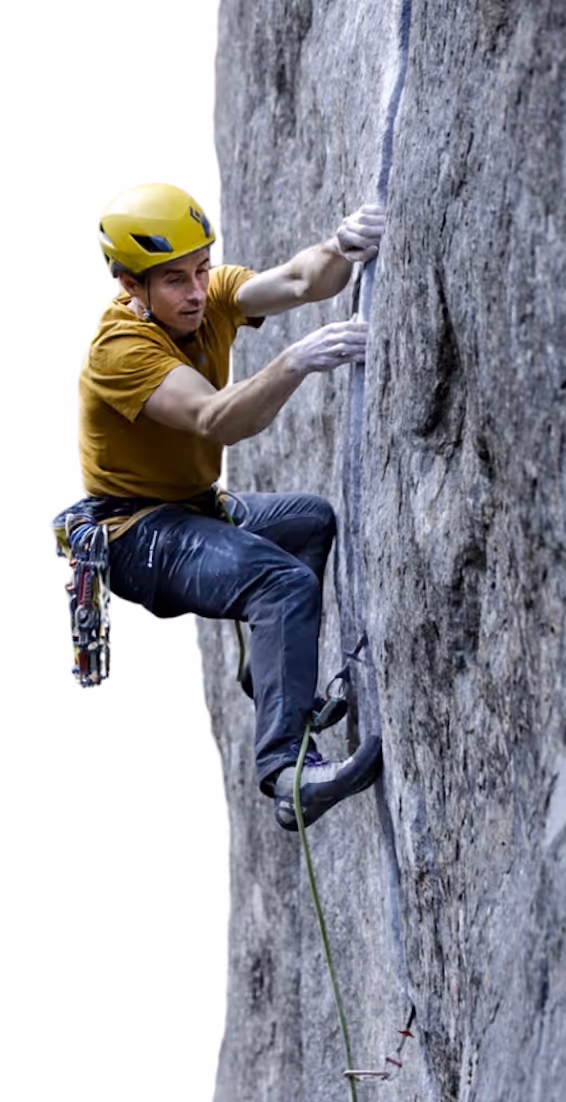 Man wearing a yellow helmet and brown shirt rock climbing a steep gray cliff using safety gear and chalked hands.