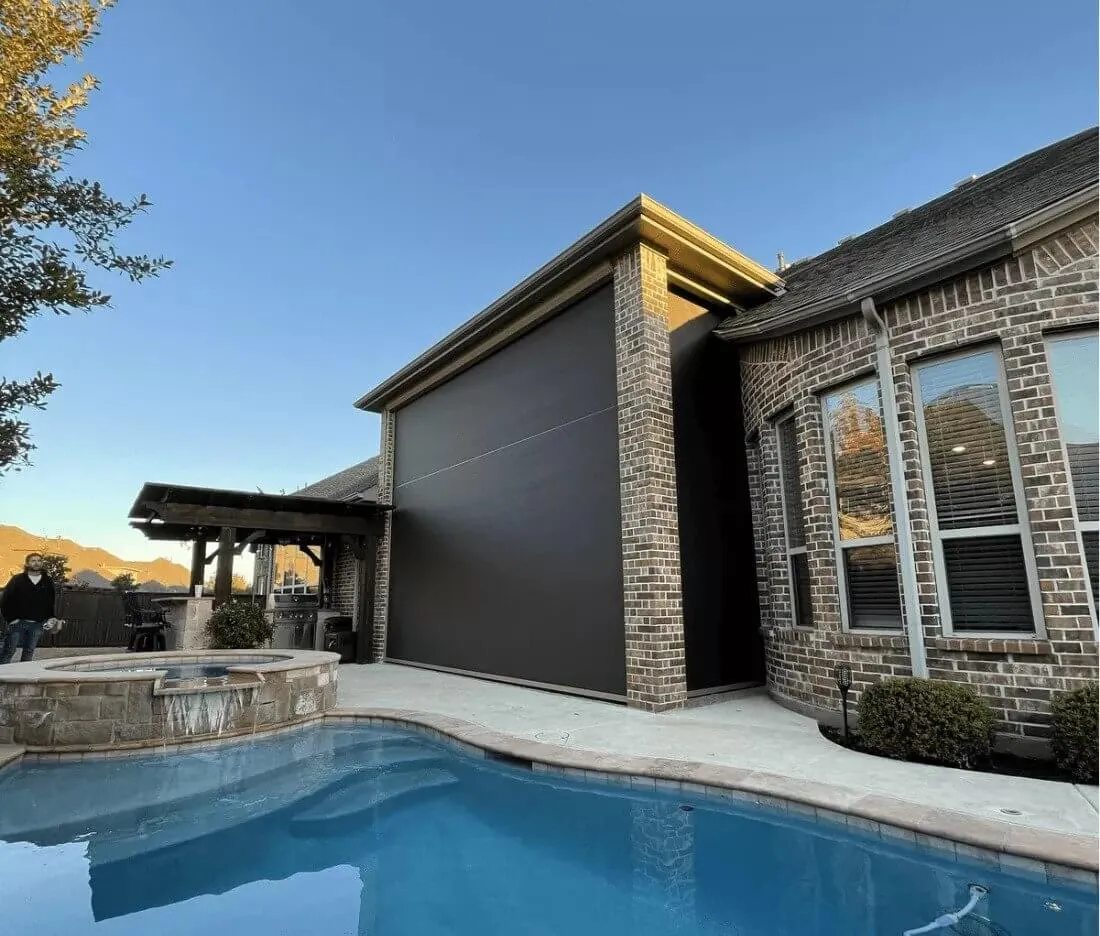 Brick house with large outdoor patio shade by a pool.