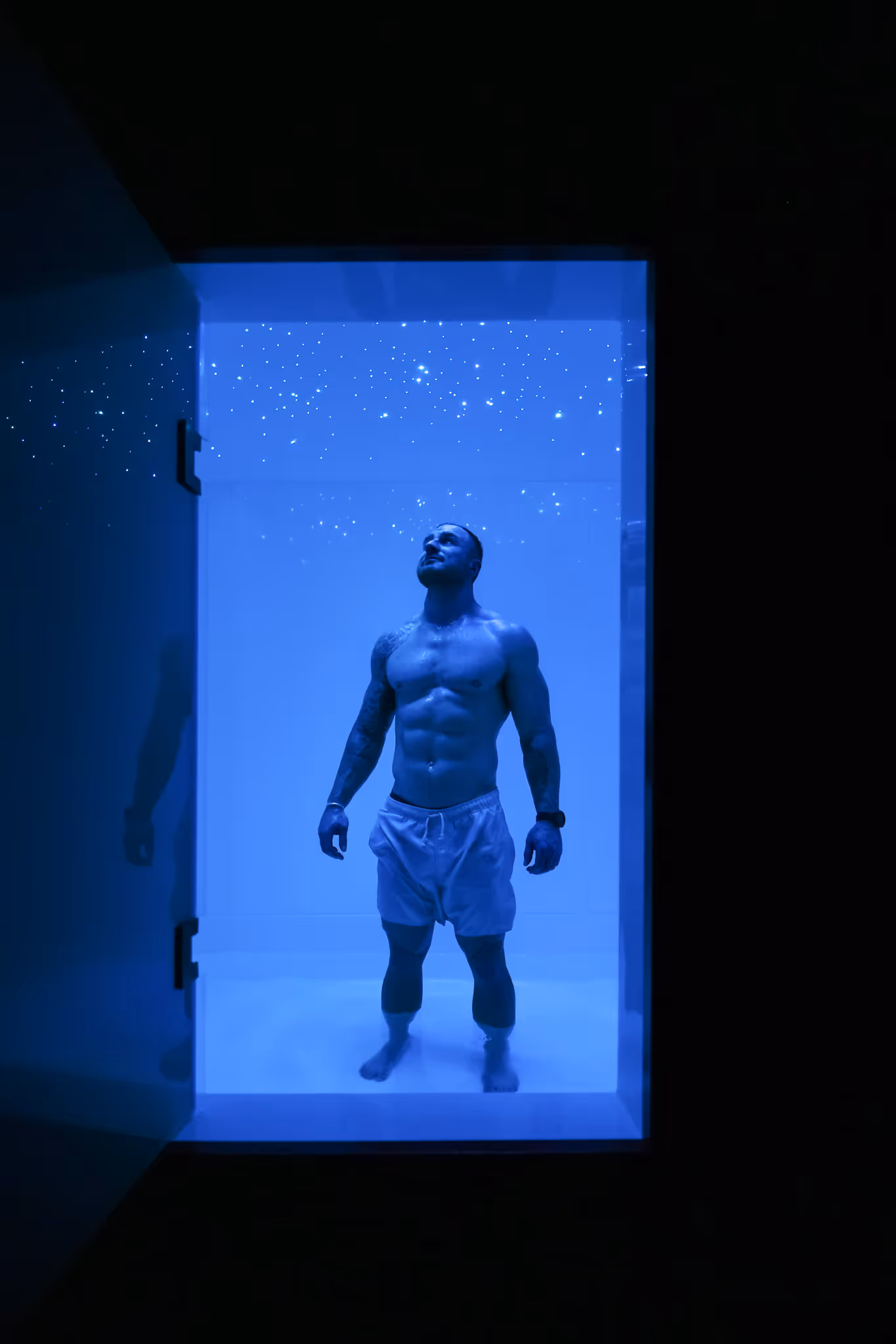 A man experiencing a float therapy session in a blue-lit float tank at O Studio, designed for deep relaxation and sensory recovery.