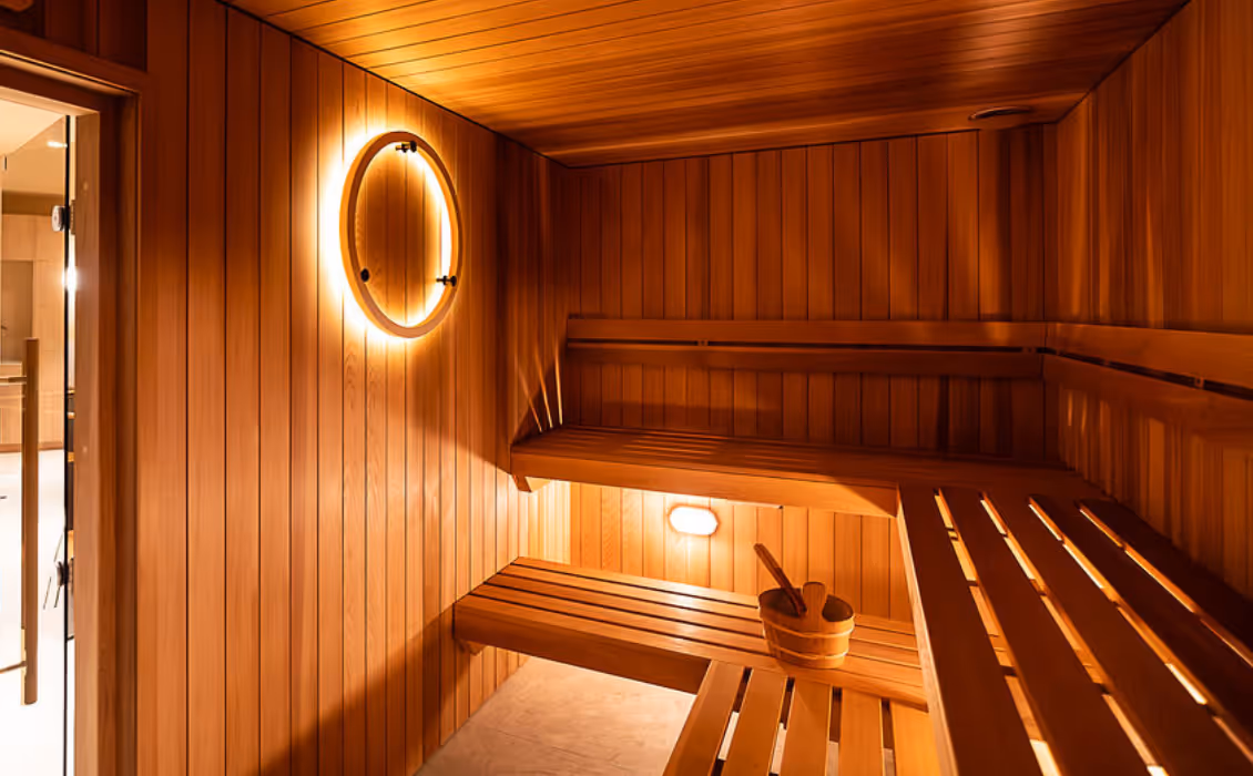 Interior of a modern wooden sauna room at O Studio, equipped with benches, a bucket, and warm lighting for relaxation and heat therapy.