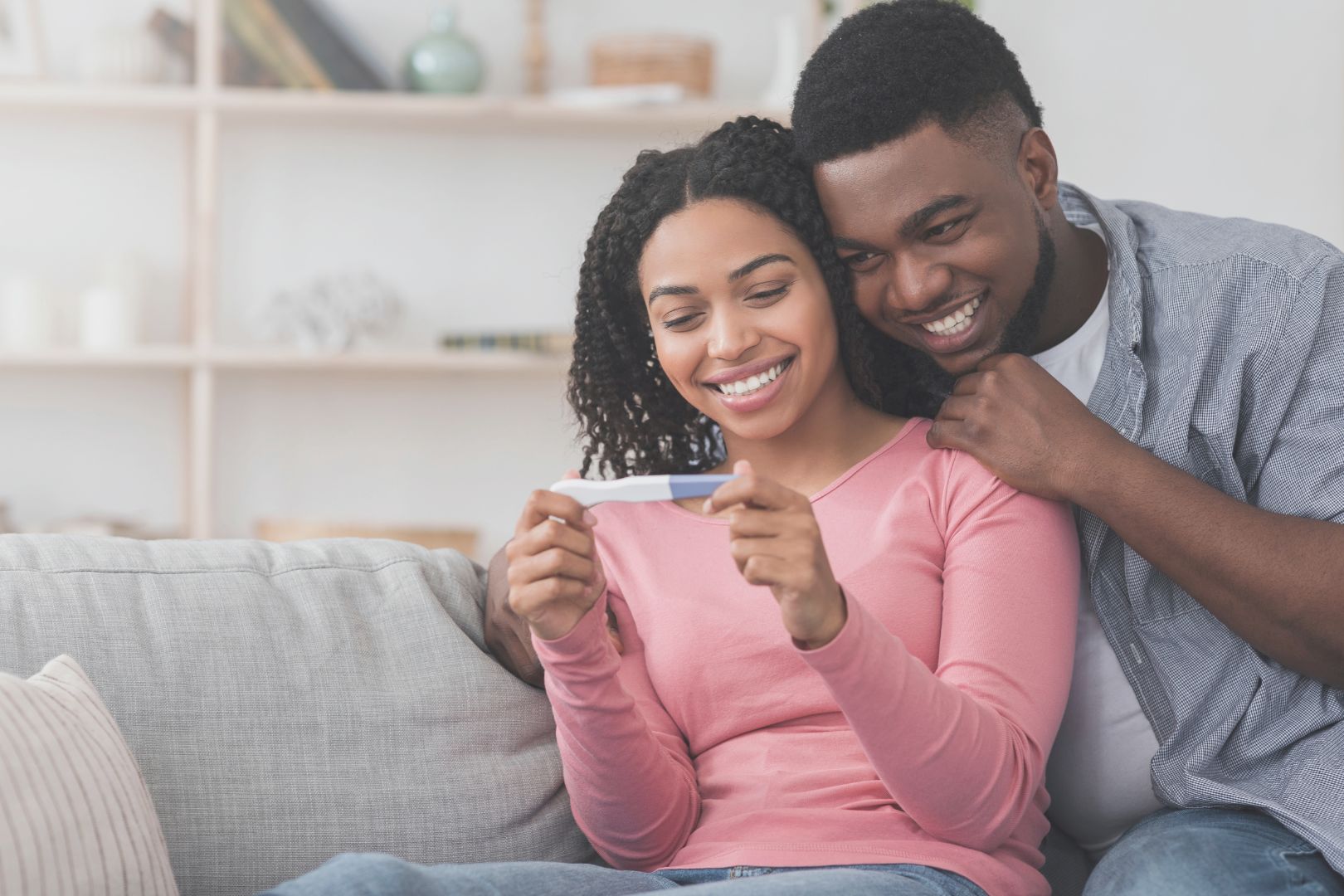 Black couple sitting on a sofa smiling at a positive pregnancy test