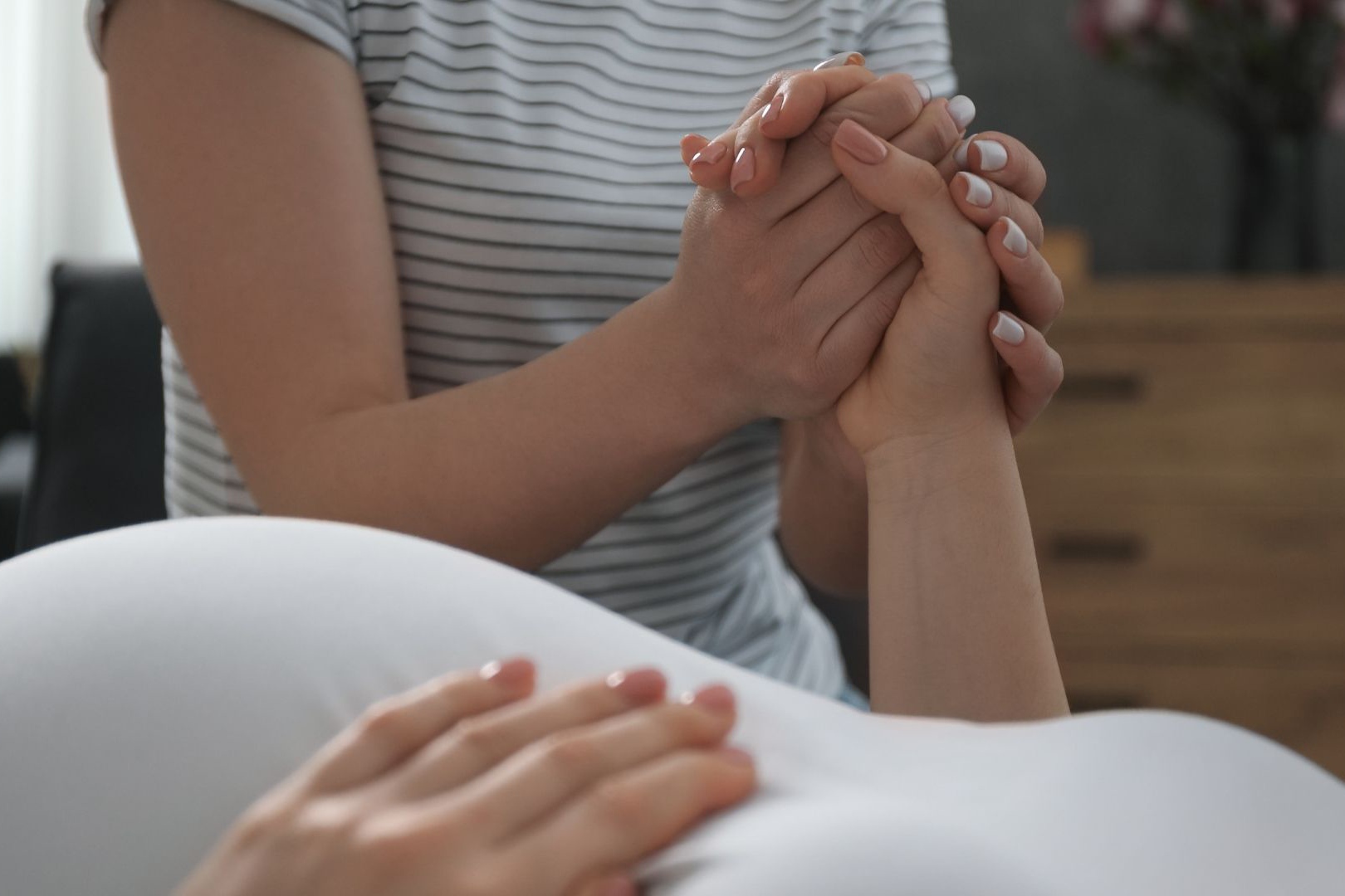 doula holding the hand of a pregnant person laying down