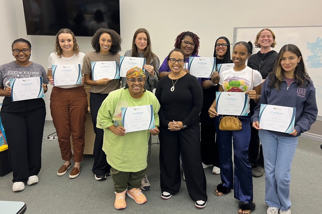 Recent graduates from a doula training program pose for a photo with their certification