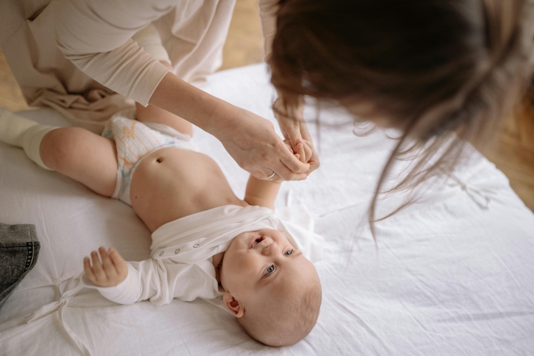 a baby looks up at a caretaker from a changing table
