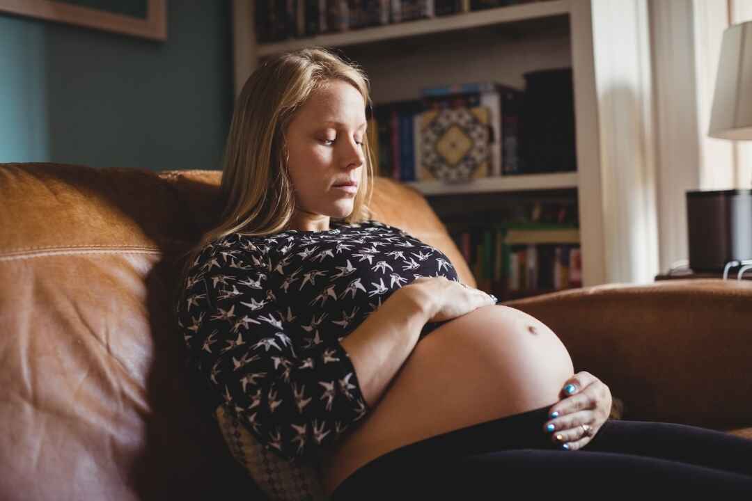 Pregnant woman sits on leather couch holding belly