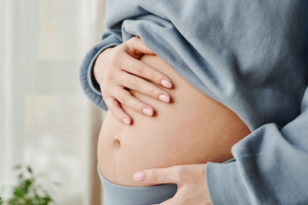 A woman wearing soft clothes holds her exposed belly