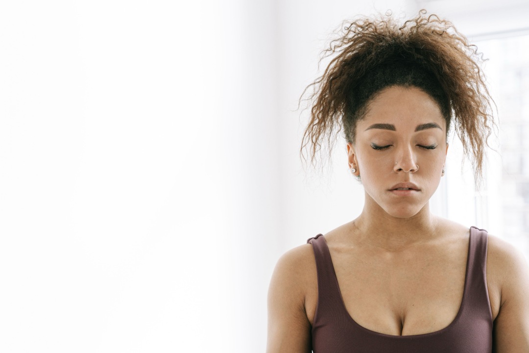 A woman stands with her eyes closed, shoulders relaxed, hair messy, as she breathes in slowly