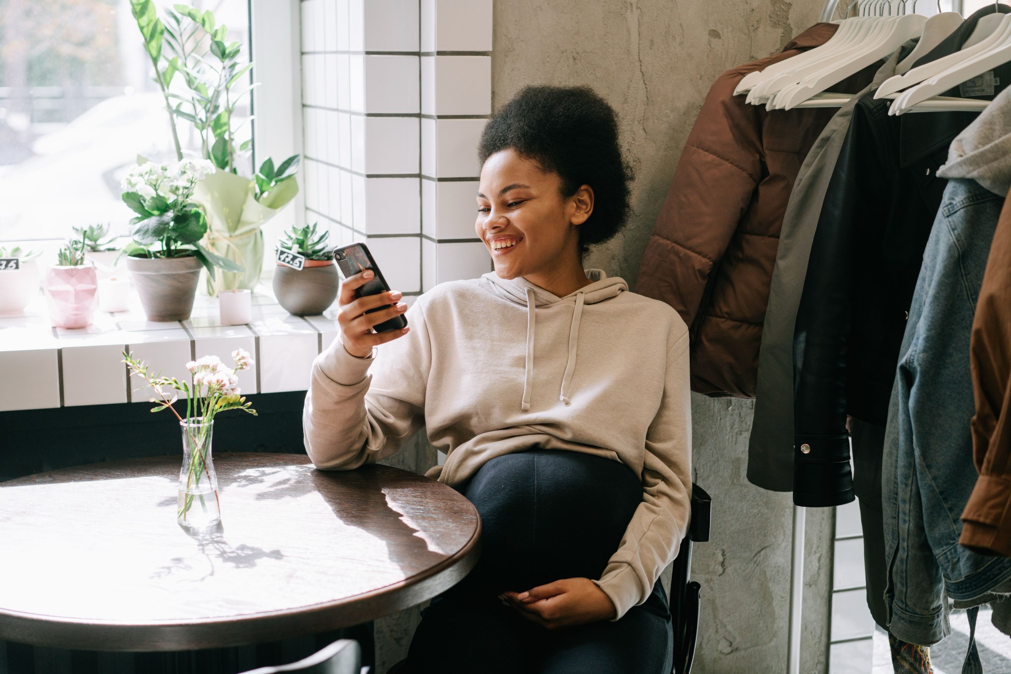 Pregnant woman sitting at a small round table, smiling and reading something on her phone