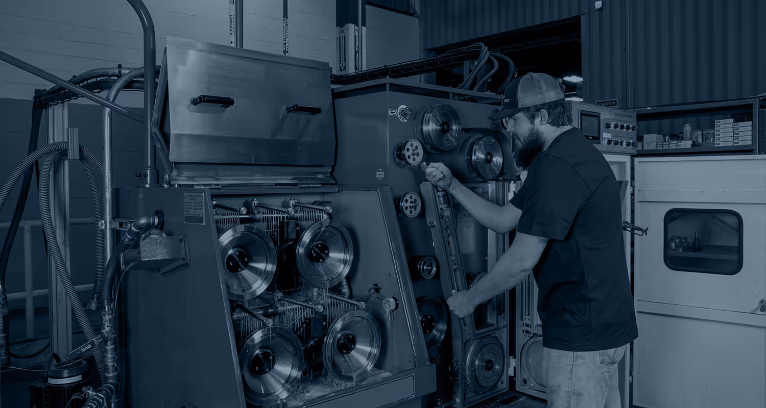 Man adjusting knobs on large industrial wire cable machine in a workshop.