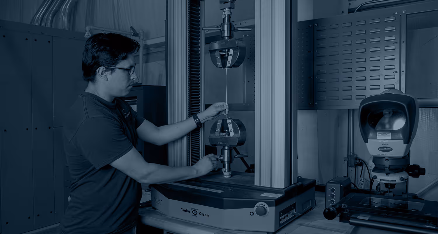 Technician adjusting metal wire in a Tinius Olsen material testing machine in a lab setting.