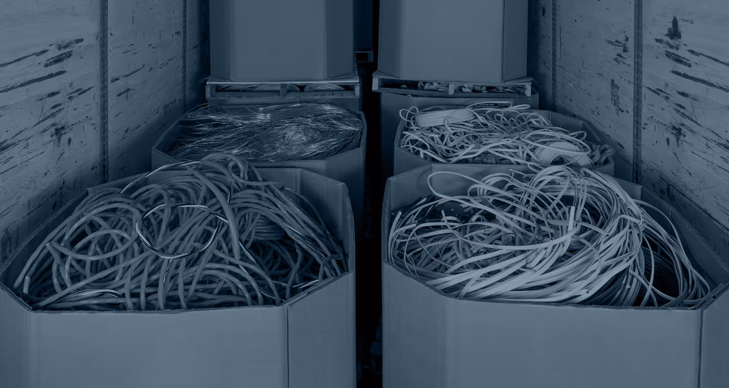 Four large containers filled with tangled electrical cables inside a storage space with scratched walls.