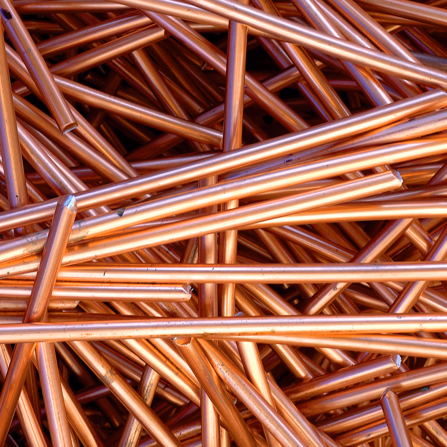 Pile of shiny, cut copper pipes interwoven in a dense stack.