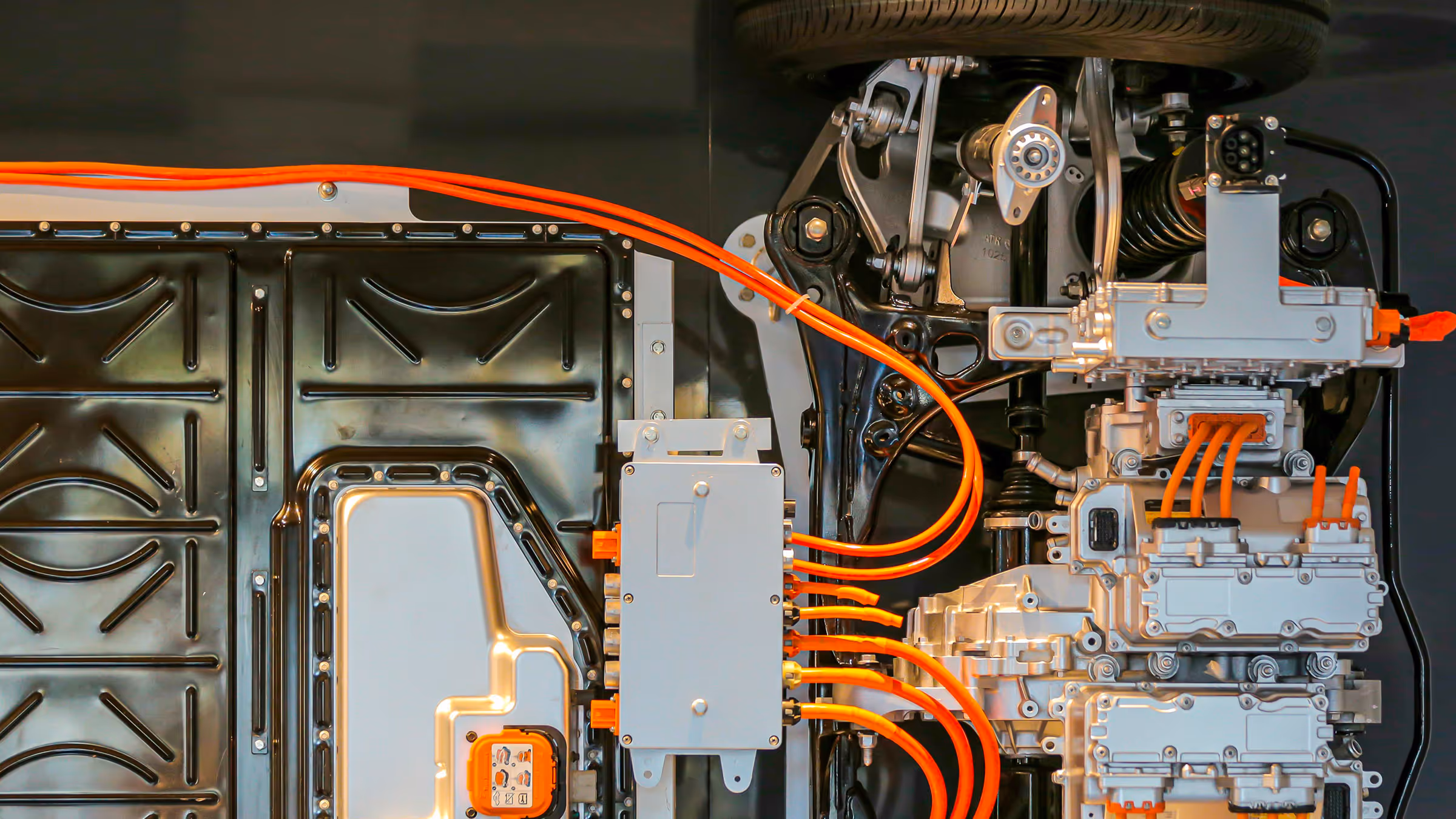 Close-up of electric vehicle components with metal parts and bright orange high-voltage cables.