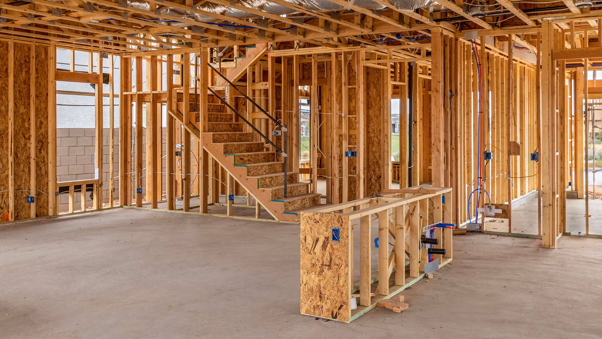 Interior of a wooden-framed house under construction with exposed studs and a staircase.
