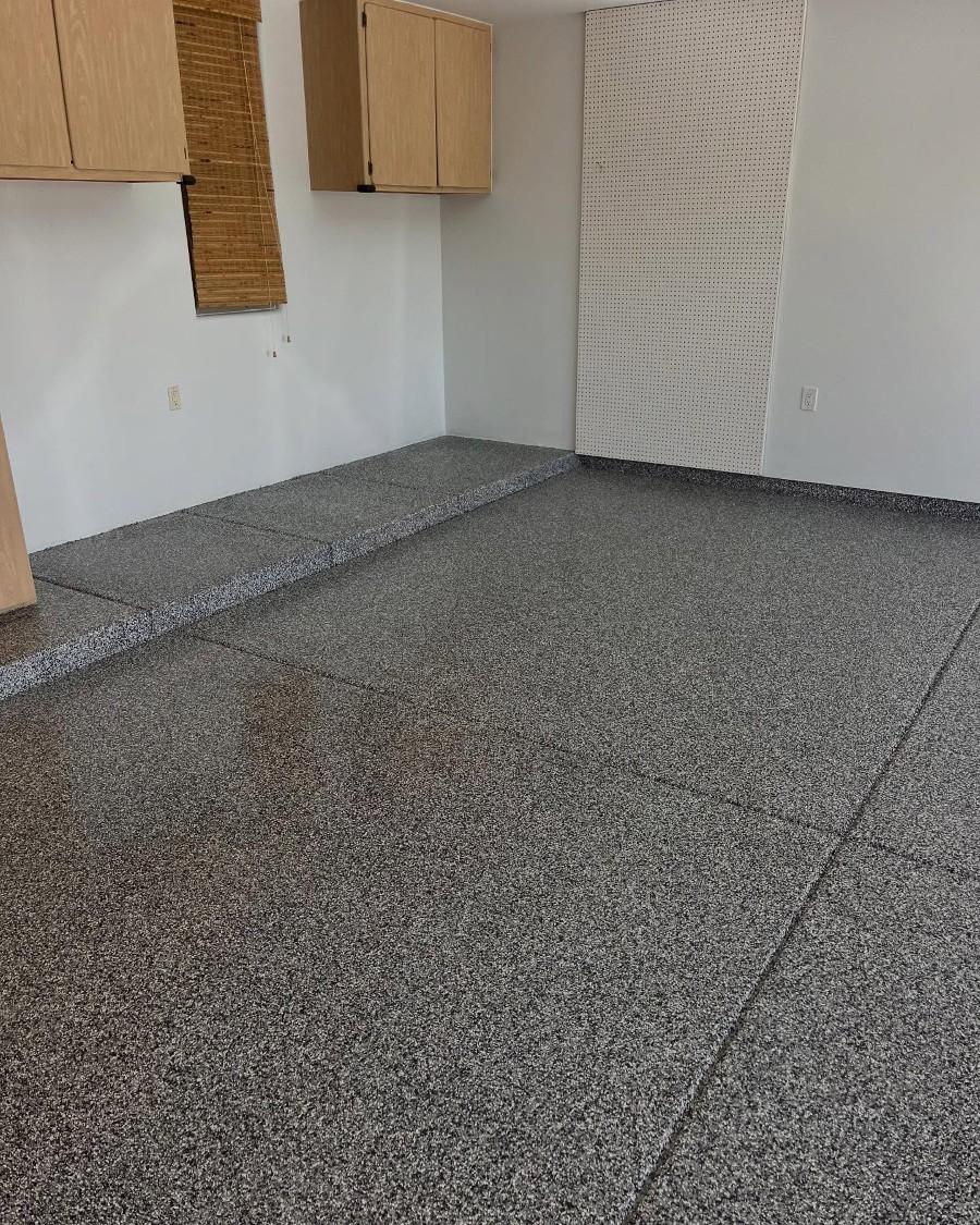 Clean garage interior with newly installed gray epoxy flake flooring, wooden cabinets, and a small elevated platform.