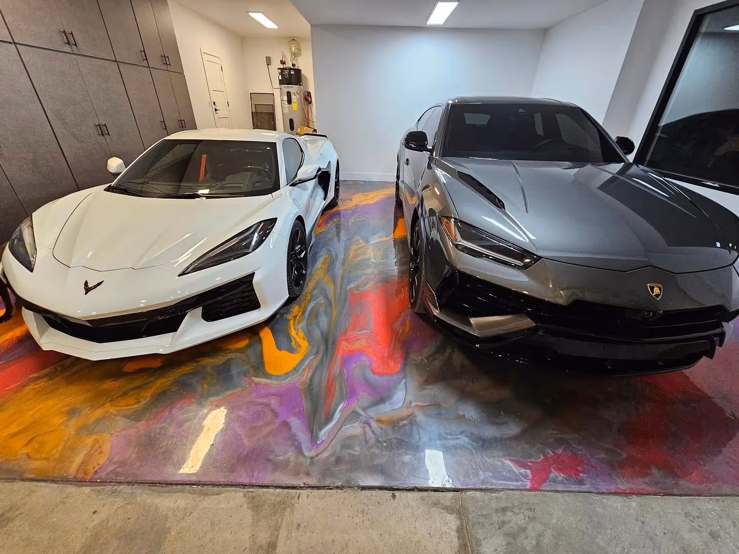 White Chevrolet Corvette and gray Lamborghini parked side by side on a multi-colored metallic epoxy garage floor.