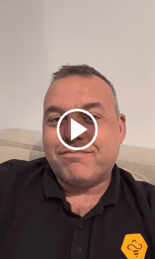 Man in a black shirt with a yellow bee logo smiling slightly while sitting on a beige couch.