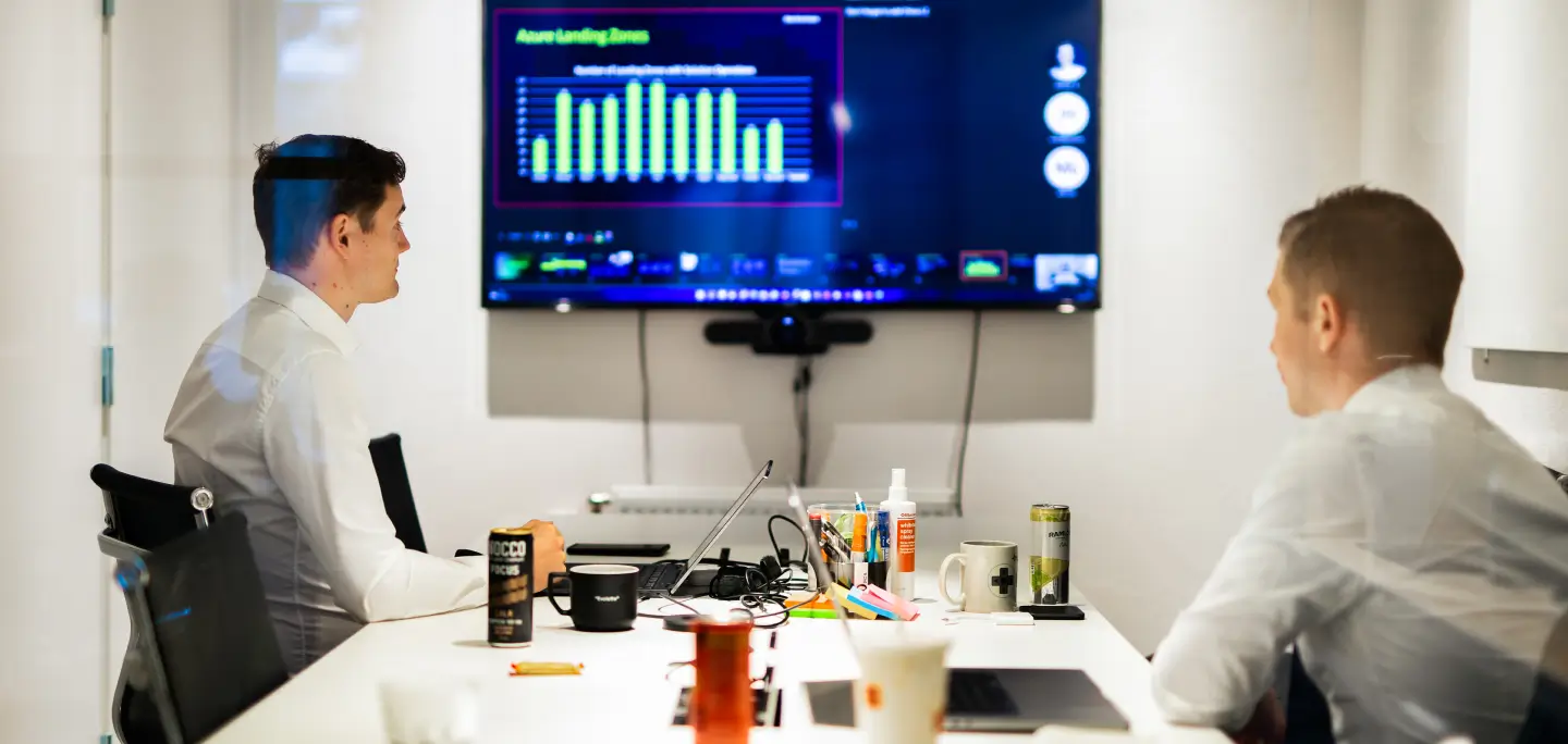 Two males sitting around a table looking at a screen at the far end