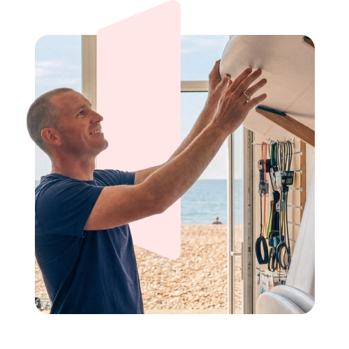 man setting up a surf board on a shelf with beach in the background