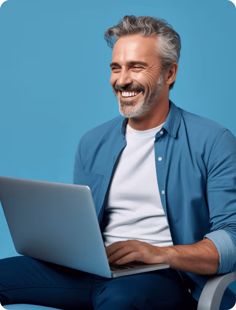 Smiling middle-aged man with gray hair sitting and using a laptop against a blue background.
