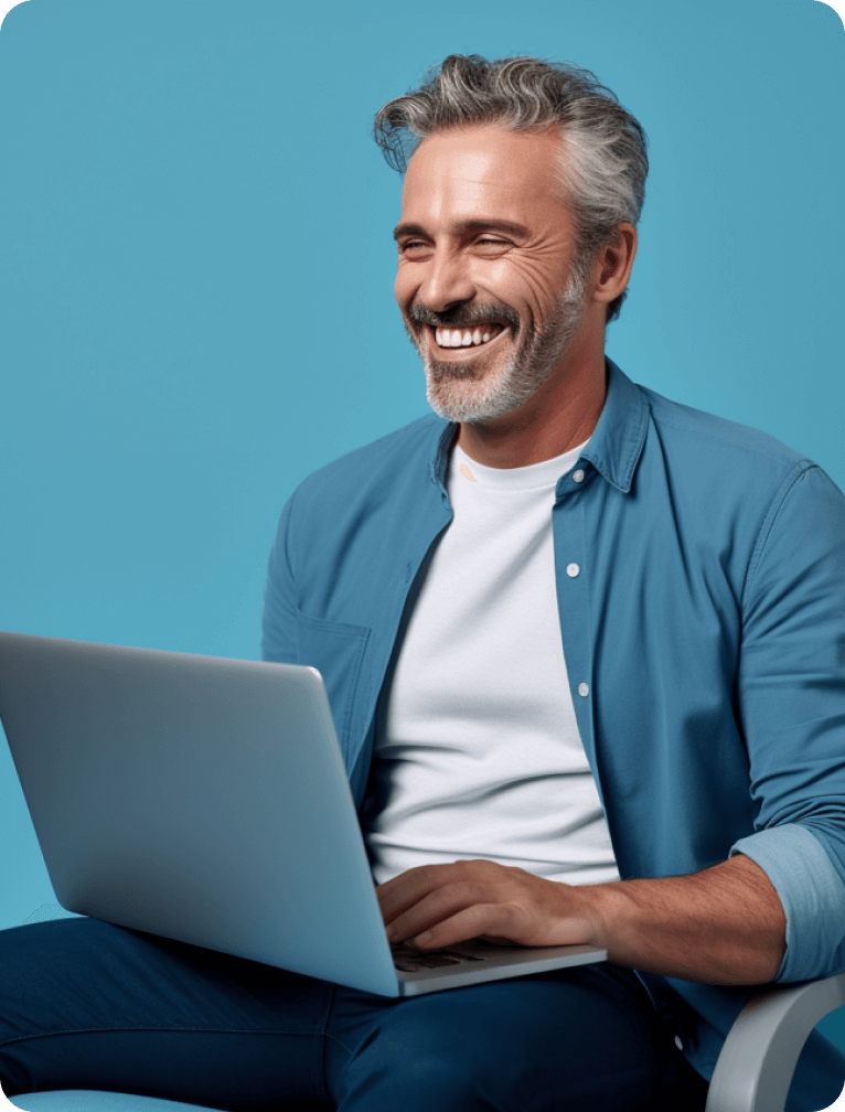 Smiling middle-aged man with gray hair sitting and using a laptop against a blue background.