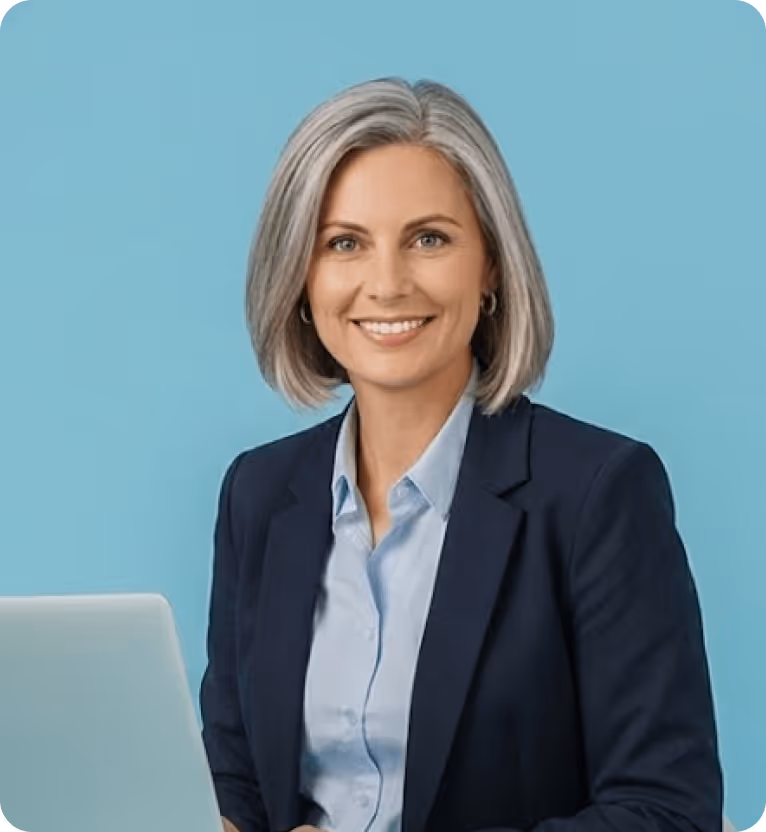 Smiling middle-aged woman with gray hair wearing a navy blazer and light blue shirt sitting in front of a laptop against a blue background.