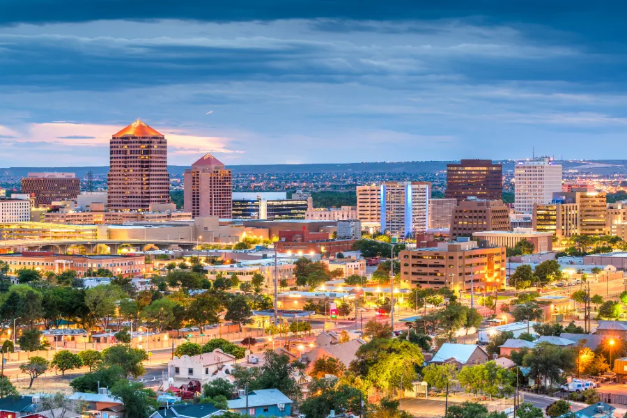 Albuquerque city skyline at dusk with illuminated buildings and a cloudy sky.