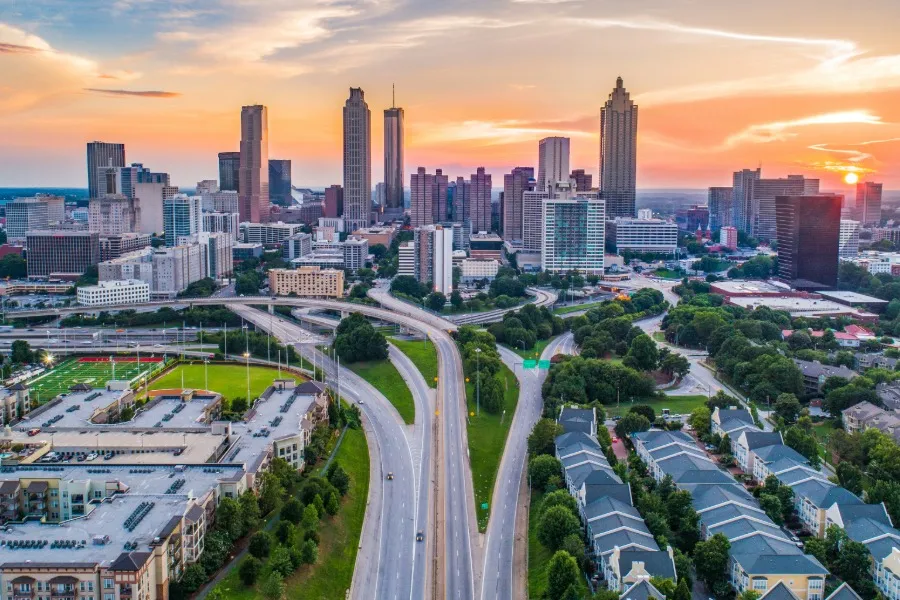 Aerial view of Atlanta, Georgia skyline at sunset with highways, trees, and residential buildings in the foreground.