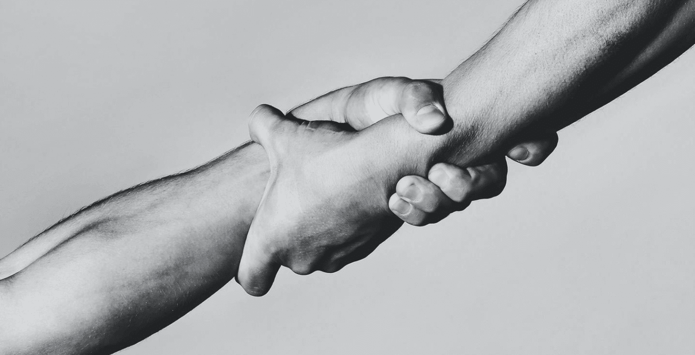 Black and white close-up of two people gripping each other's wrists in a supportive handshake.