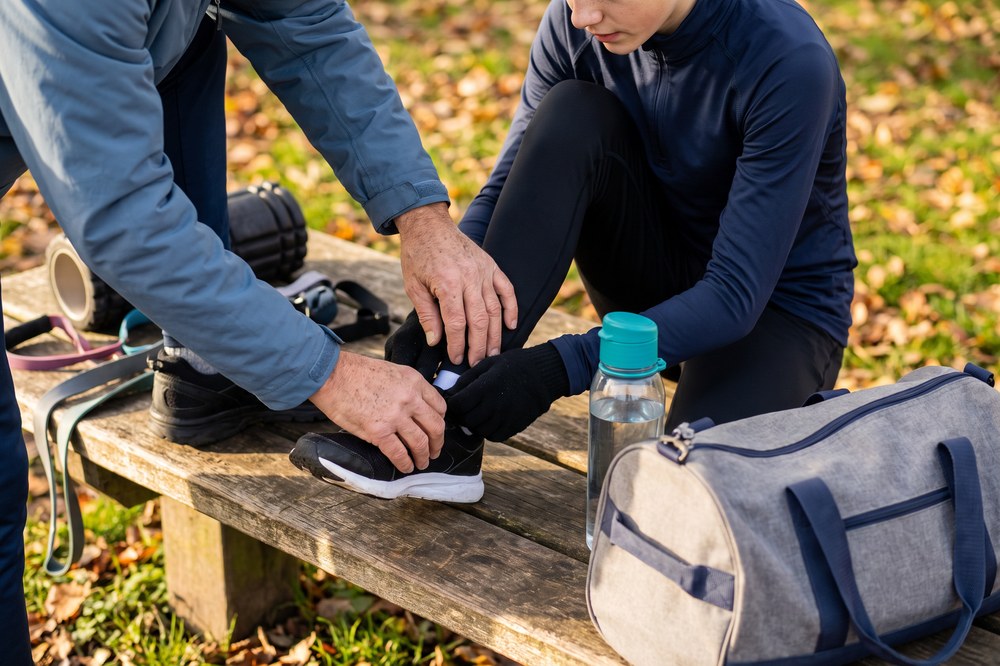 Young athlete and adult preparing a sports shoe with hydration and recovery gear nearby