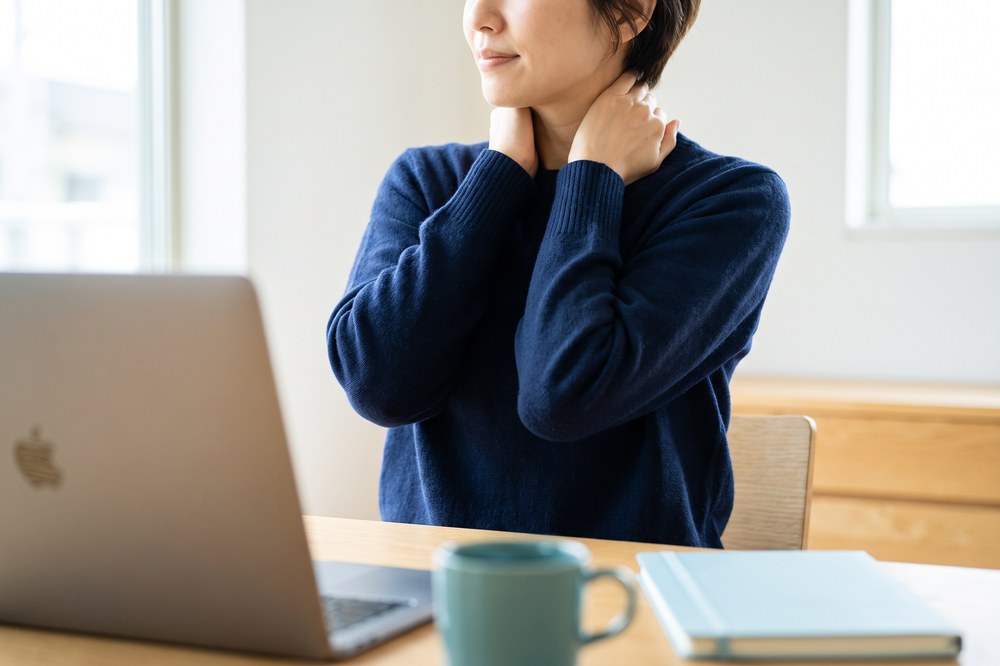 Remote worker taking a gentle neck and shoulder break beside a laptop