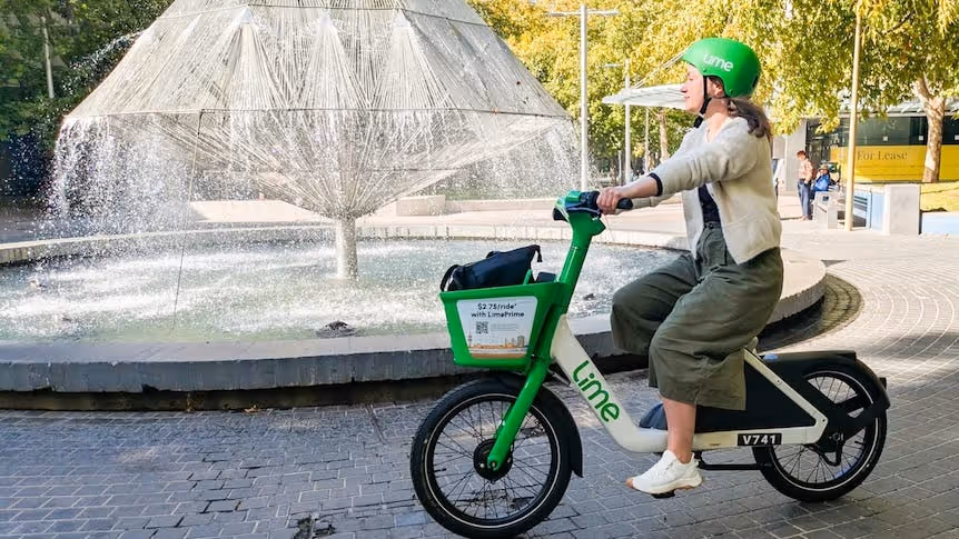 A person rides a green Lime bike near a fountain in an urban space.